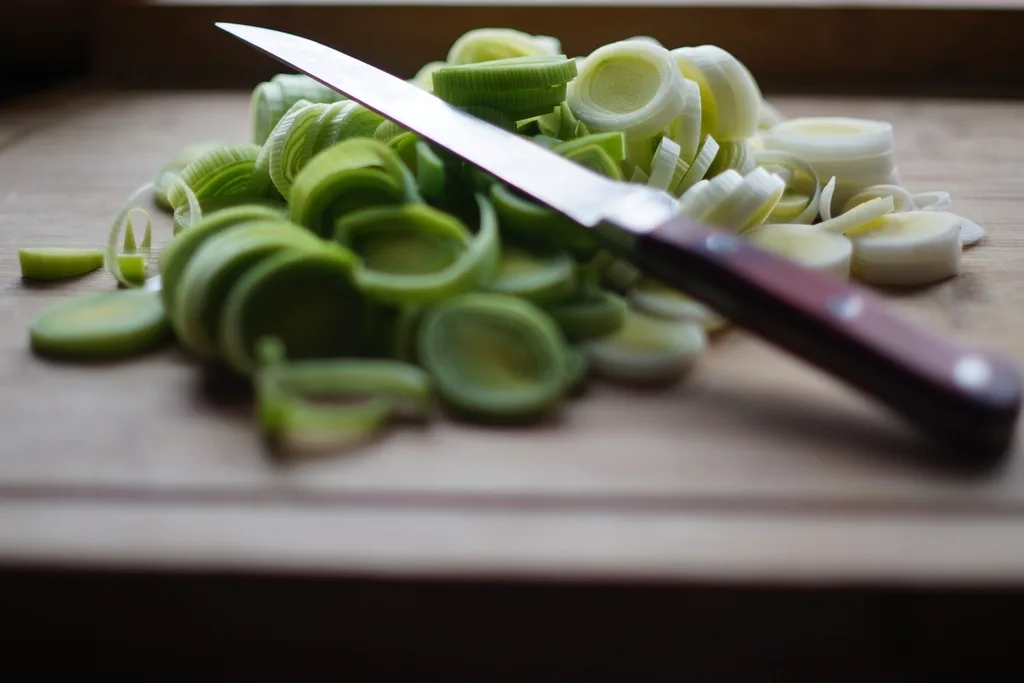 Chef knife slicing leeks on a cutting board