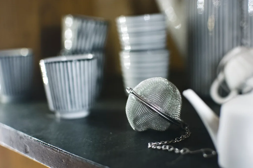 Stainless steel ball tea infuser next to a teapot and cups