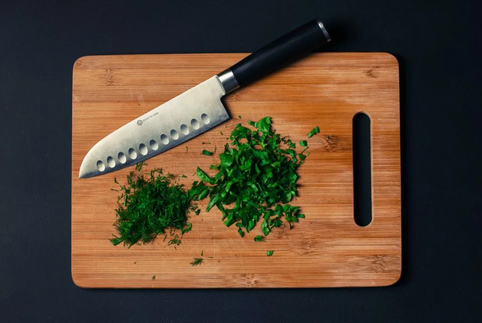 Wooden cutting board with a chef knife and chopped herbs